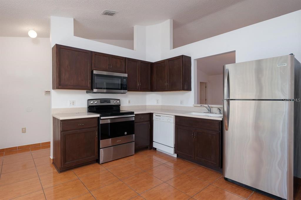 A kitchen with dark wood cabinets, stainless steel appliances, and orange tile flooring — 718 PINCON LANE, KISSIMMEE, FL