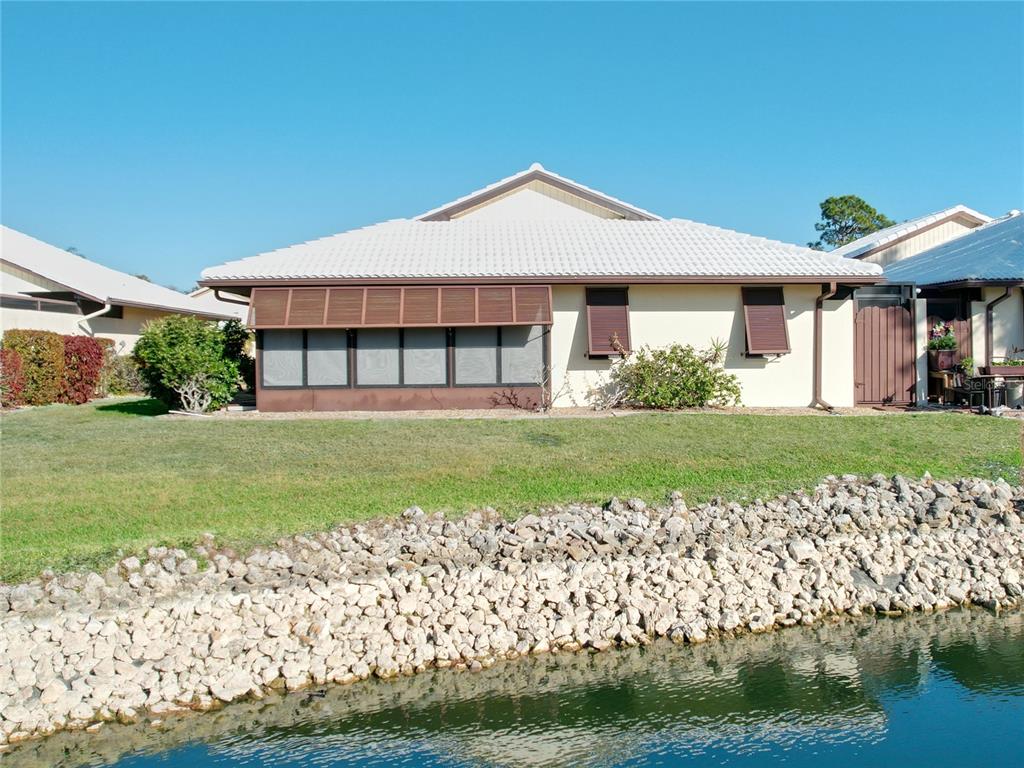 A single-story house with a screened-in porch sits along a rocky shoreline by water — 137 DRIFTING SANDS DRIVE, VENICE, FL