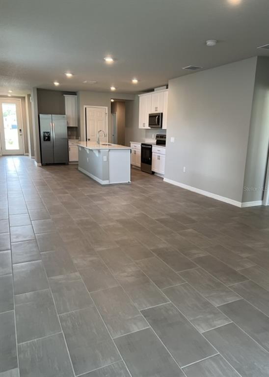 An open-concept kitchen features white cabinetry, stainless steel appliances, a center island, and tile flooring — 953 RIVERS CROSSING STREET, CLERMONT, FL