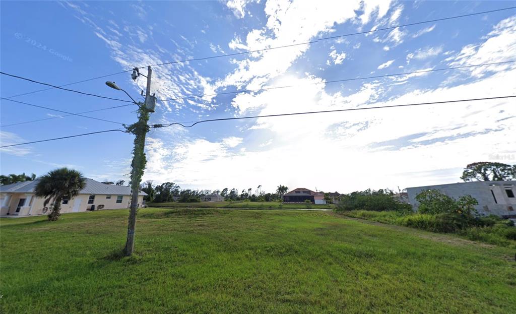 A grassy vacant lot sits between two houses under a bright, cloudy sky — 243 TOURNAMENT ROAD, ROTONDA WEST, FL