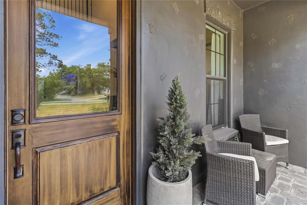 A wooden front door opens onto a covered porch with dark walls and wicker seating — 6805 BASS HIGHWAY, ST CLOUD, FL