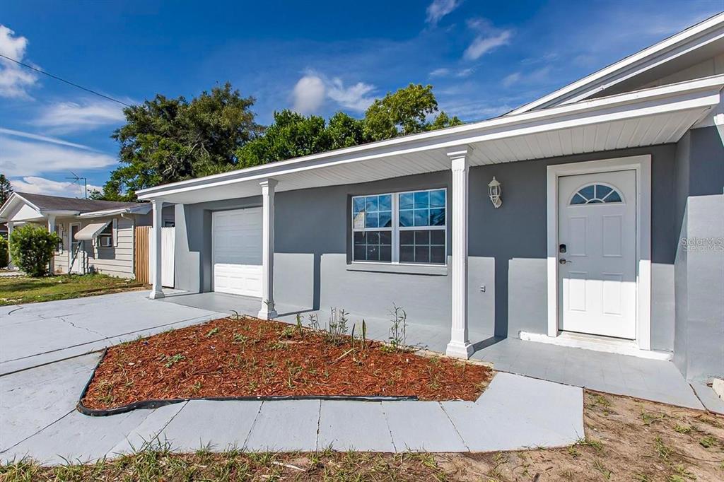A gray single-story house with a white front door, a garage, and a mulched garden — 3549 WINDER DRIVE, HOLIDAY, FL