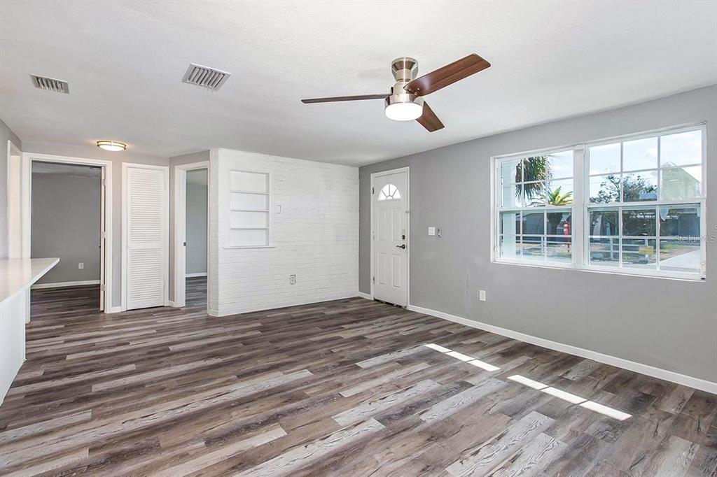 A living room with gray walls, wood-look flooring, a ceiling fan, and a white brick wall — 3549 WINDER DRIVE, HOLIDAY, FL
