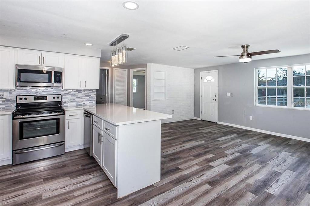 A kitchen with white cabinets, stainless steel appliances, and an island opens to a living area — 3549 WINDER DRIVE, HOLIDAY, FL