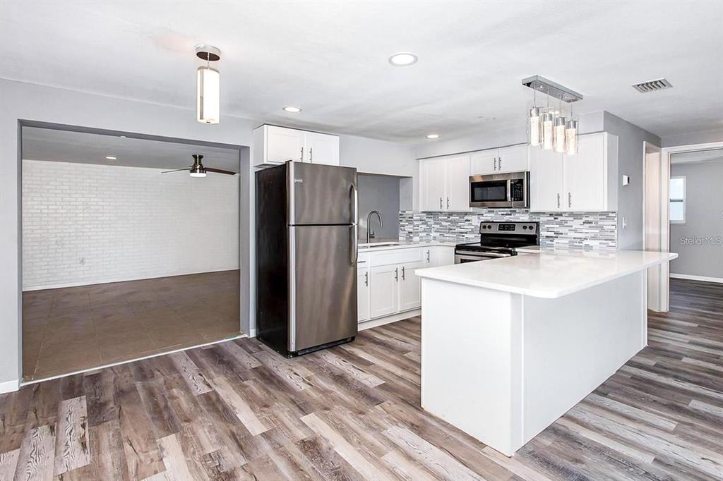 A kitchen with white cabinets, stainless steel appliances, and a white island on wood flooring — 3549 WINDER DRIVE, HOLIDAY, FL
