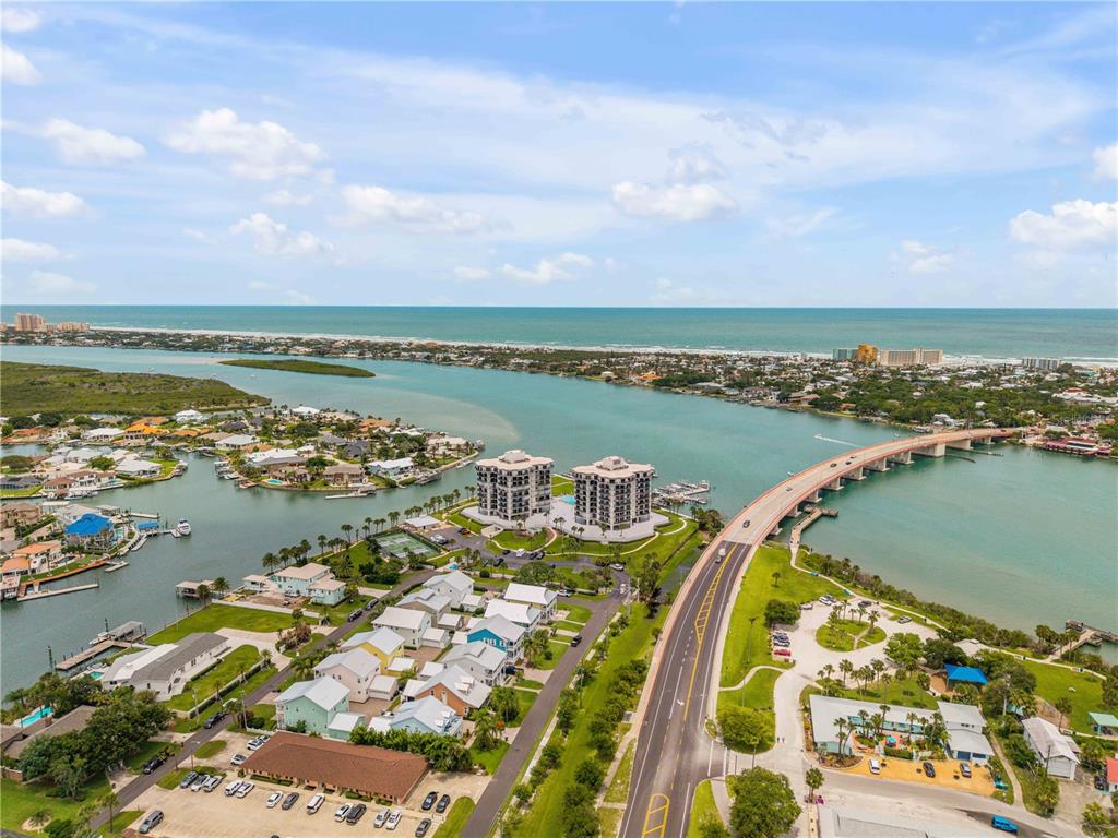 An aerial view shows a coastal area with a bridge, residential homes, and two high-rise buildings — 503 N CAUSEWAY UNIT 1020, NEW SMYRNA BEACH, FL