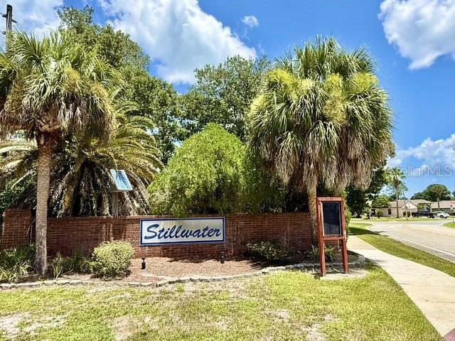 A brick wall with a Stillwater sign stands before palm trees and a paved road — 553 WALNUT GROVE PLACE, OVIEDO, FL