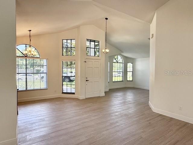 A bright, open-concept living area features light wood-look flooring, vaulted ceilings, and multiple windows — 553 WALNUT GROVE PLACE, OVIEDO, FL