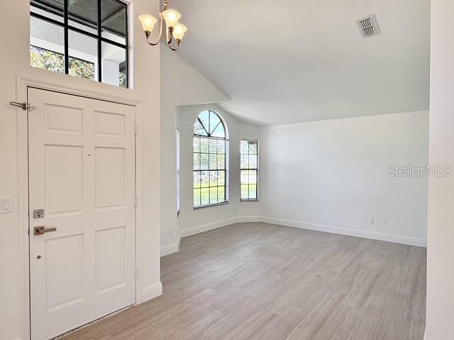 An entryway with a white door, light wood-look flooring, and a vaulted ceiling — 553 WALNUT GROVE PLACE, OVIEDO, FL