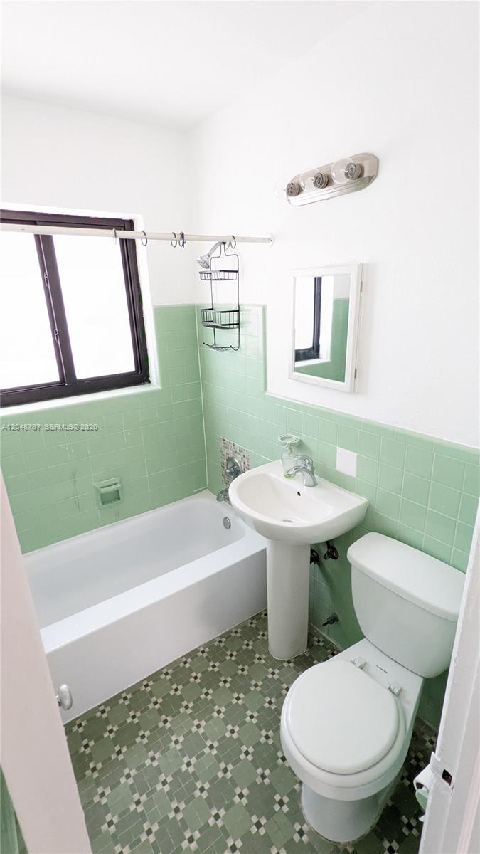 A bathroom features a white bathtub, pedestal sink, toilet, and green tiled walls — 811 81st St # 2, Miami Beach FL 33141, MIAMI BEACH, FL