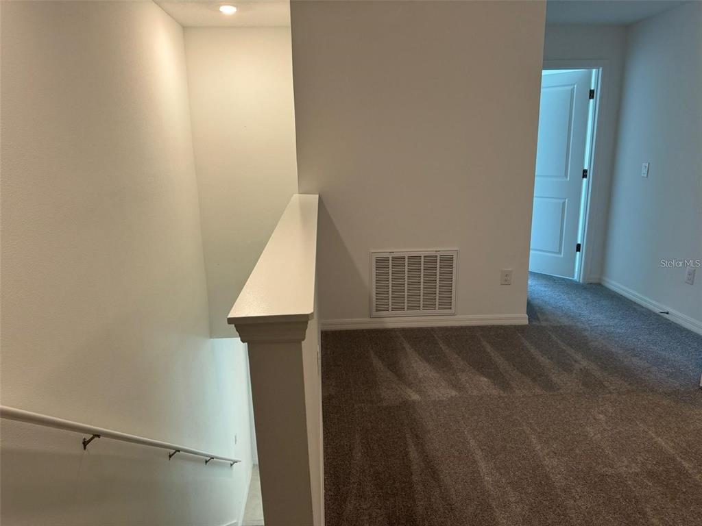 A carpeted landing features a staircase with a white railing and a wall vent — 10375 TRUMPET HONEYSUCKLE WAY, SAN ANTONIO, FL