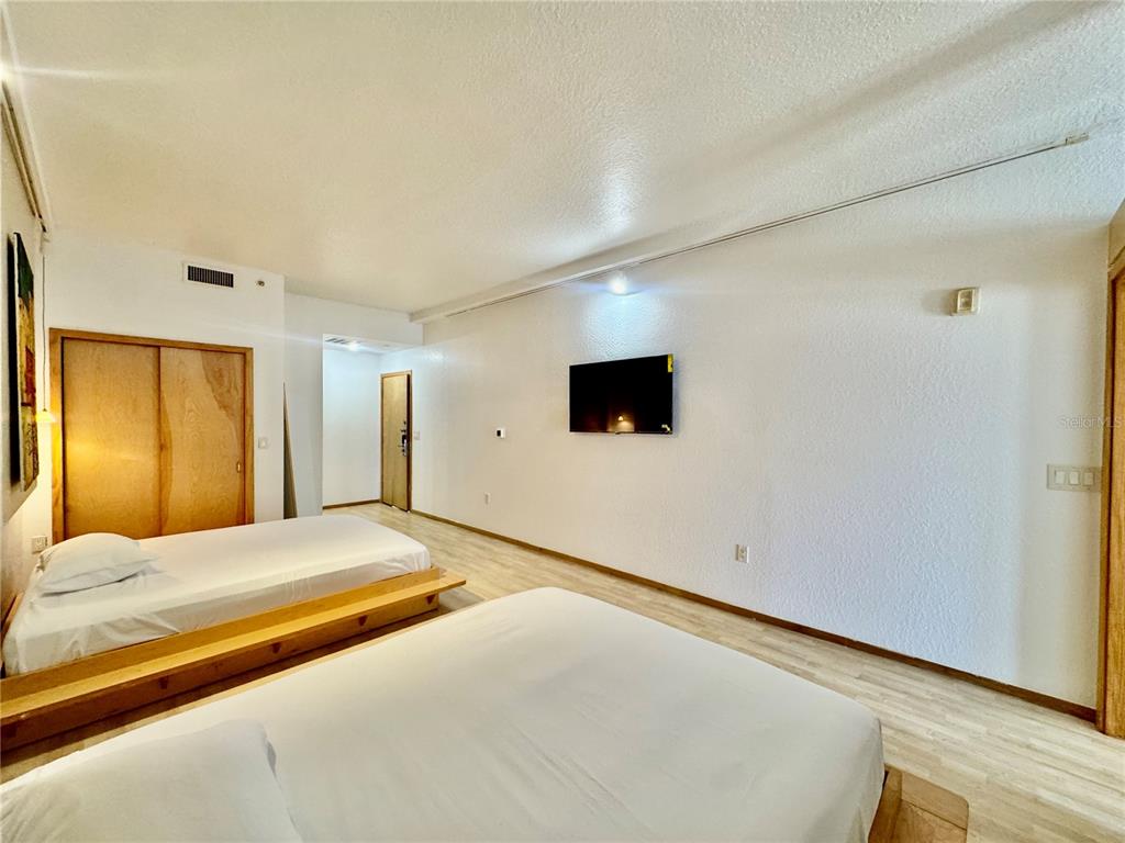 A bedroom features two beds on wooden platforms, light wood flooring, and a wall-mounted television — 101 PALM HARBOR PARKWAY UNIT B414, PALM COAST, FL