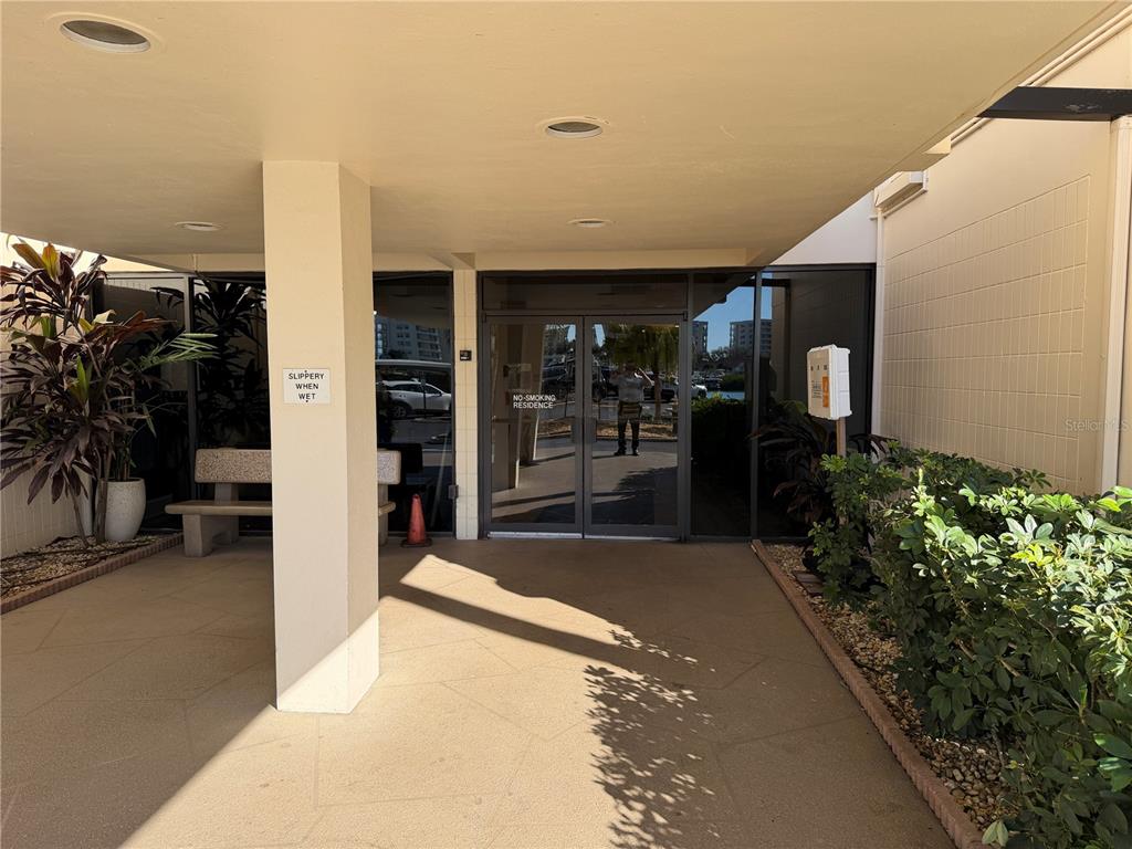 A covered building entrance features a concrete walkway, a support pillar, and glass double doors — 7400 SUN ISLAND DRIVE S UNIT 103, SOUTH PASADENA, FL