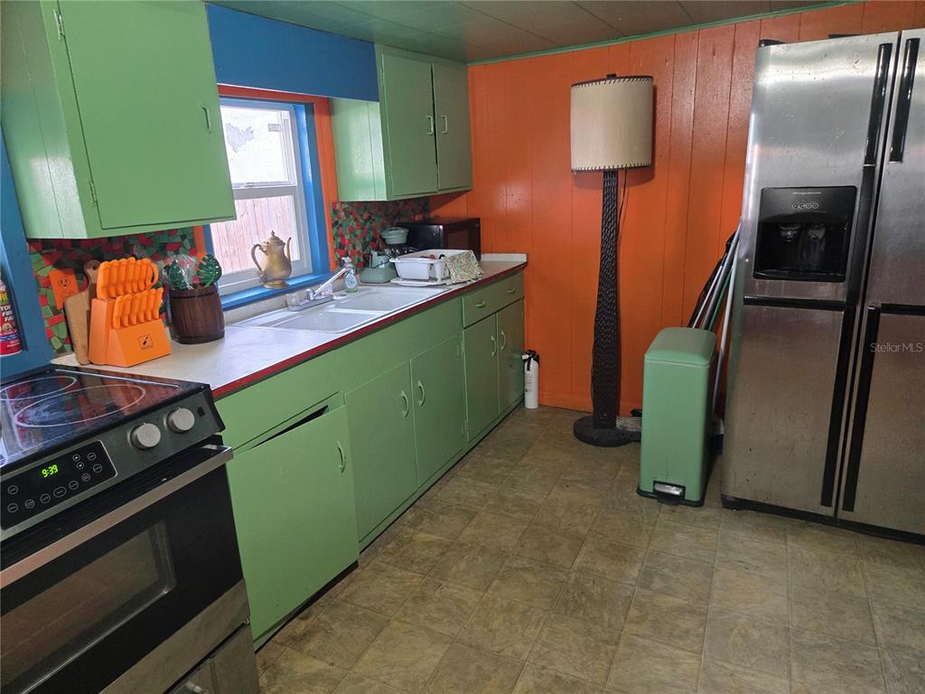 A kitchen features green cabinets, orange walls, a stainless steel refrigerator, and a floor lamp — 1407 ILLINOIS AVENUE, ST CLOUD, FL