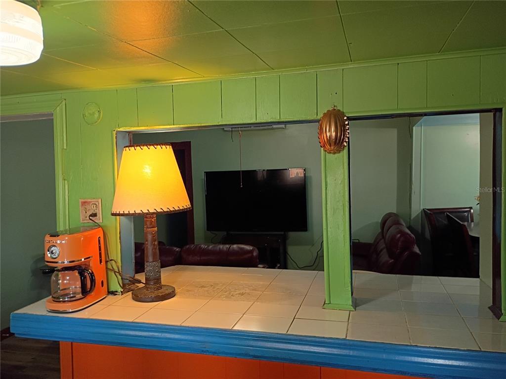 A kitchen pass-through window with a tiled counter overlooks a living room with a television — 1407 ILLINOIS AVENUE, ST CLOUD, FL