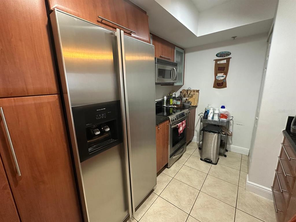 A kitchen features stainless steel appliances, wood cabinetry, and light-colored tile flooring — 3232 CORAL WAY UNIT 1607, MIAMI, FL