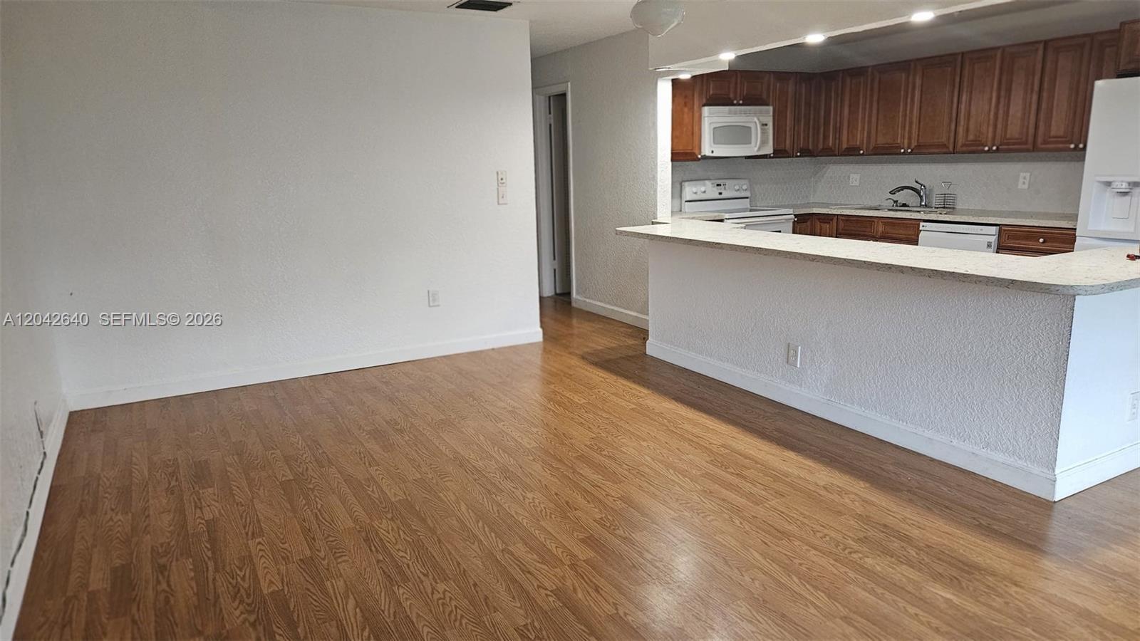 An open-concept living area features wood-look flooring and a kitchen with wood cabinets — 8555 NW 10th St # B106, Plantation FL 33322, PLANTATION, FL