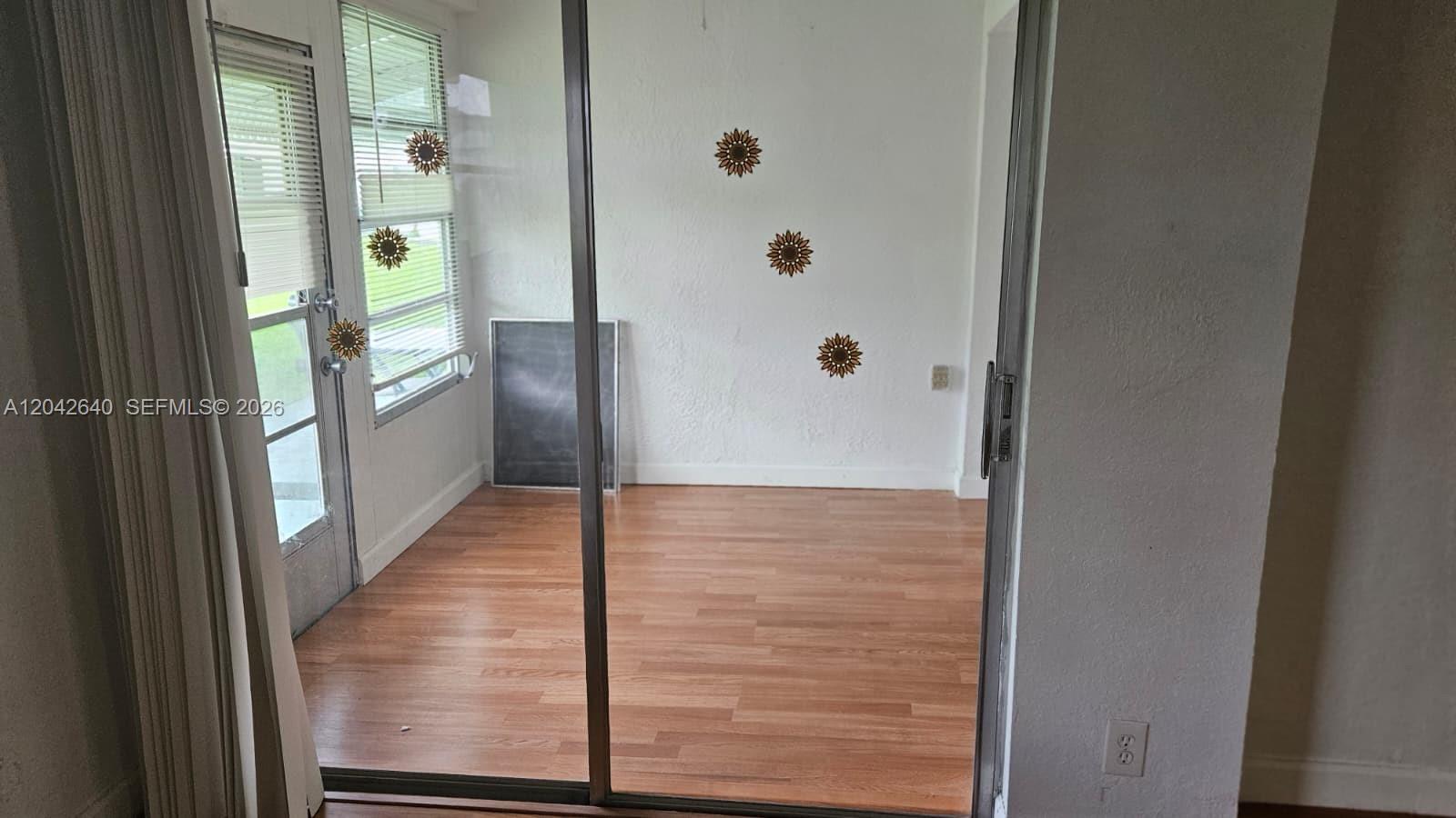 A sunroom features wood-look flooring, white walls with sunflower decor, and a glass sliding door — 8555 NW 10th St # B106, Plantation FL 33322, PLANTATION, FL