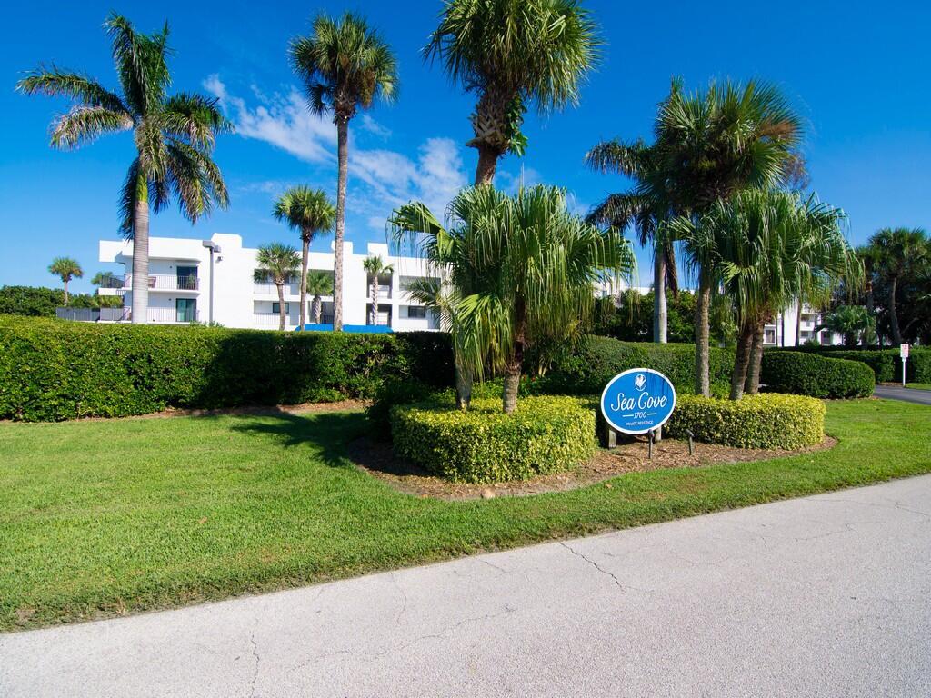 A blue sign for Sea Cove stands in front of palm trees and a white building — 1700 Ocean Drive # 306, Vero Beach FL 32963, VERO BEACH, FL