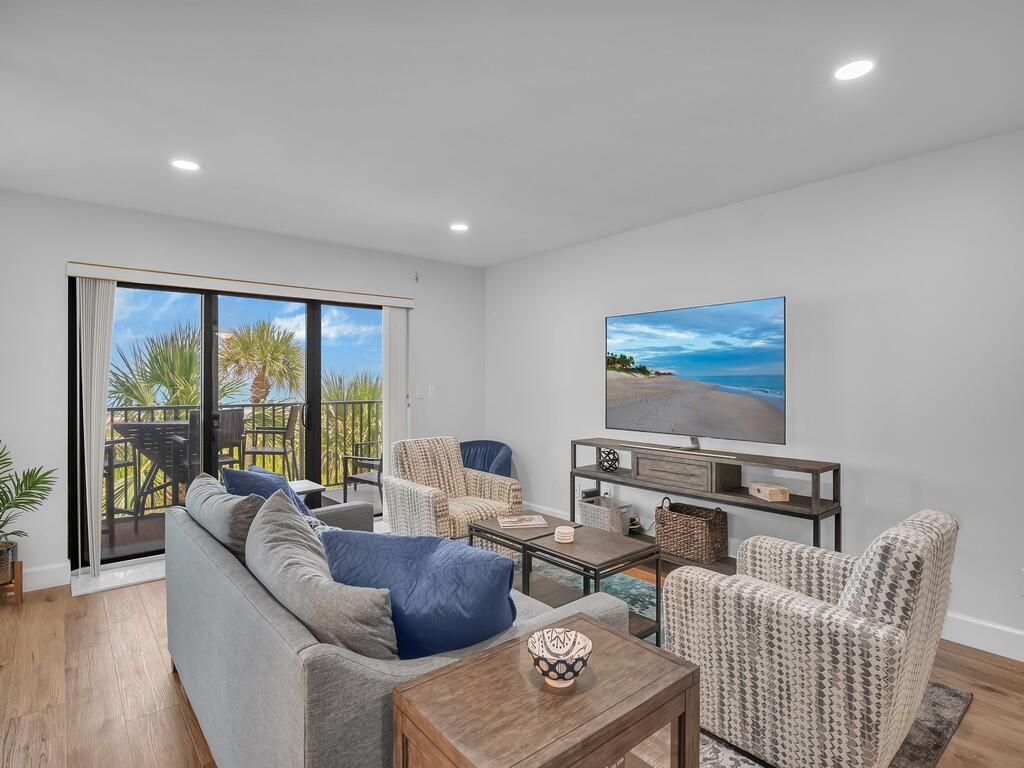 A living room features a gray sofa, two patterned armchairs, a television, and a balcony — 1700 Ocean Drive # 306, Vero Beach FL 32963, VERO BEACH, FL