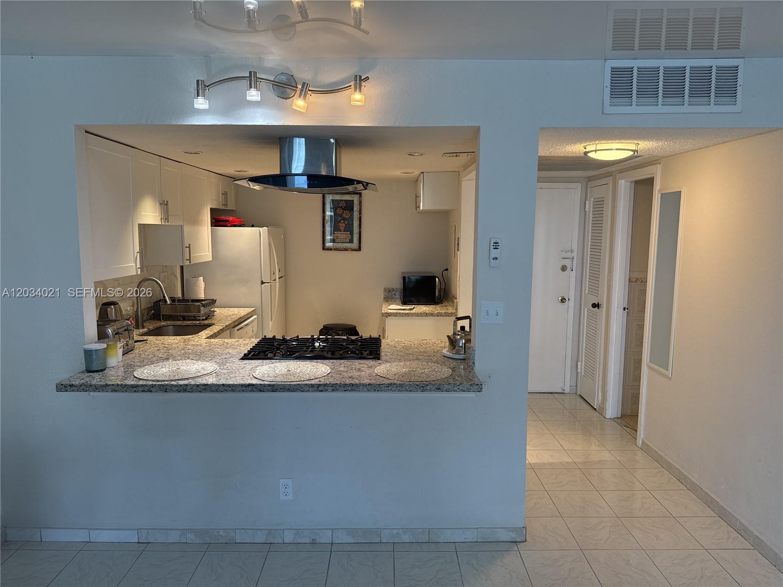 A kitchen with granite countertops and a breakfast bar opens into a tiled hallway — 2030 S Ocean Dr # 1511, Hallandale Beach FL 33009, HALLANDALE BEACH, FL