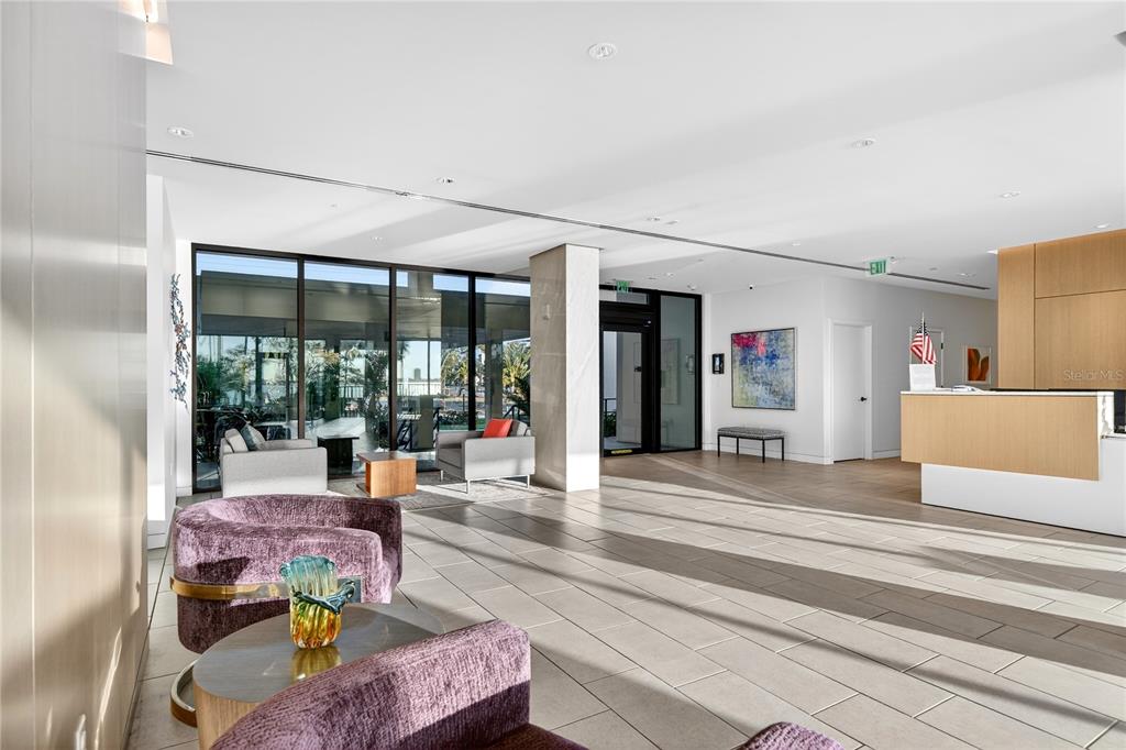 A modern lobby features purple armchairs, a reception desk, and floor-to-ceiling windows overlooking a patio — 770 S PALM AVENUE UNIT PH2, SARASOTA, FL