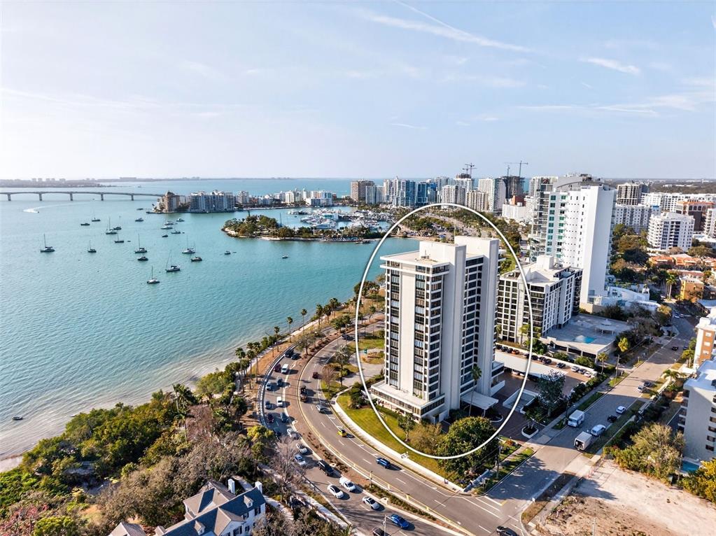 An aerial view shows a tall residential building situated along a coastal road and bay — 770 S PALM AVENUE UNIT PH2, SARASOTA, FL