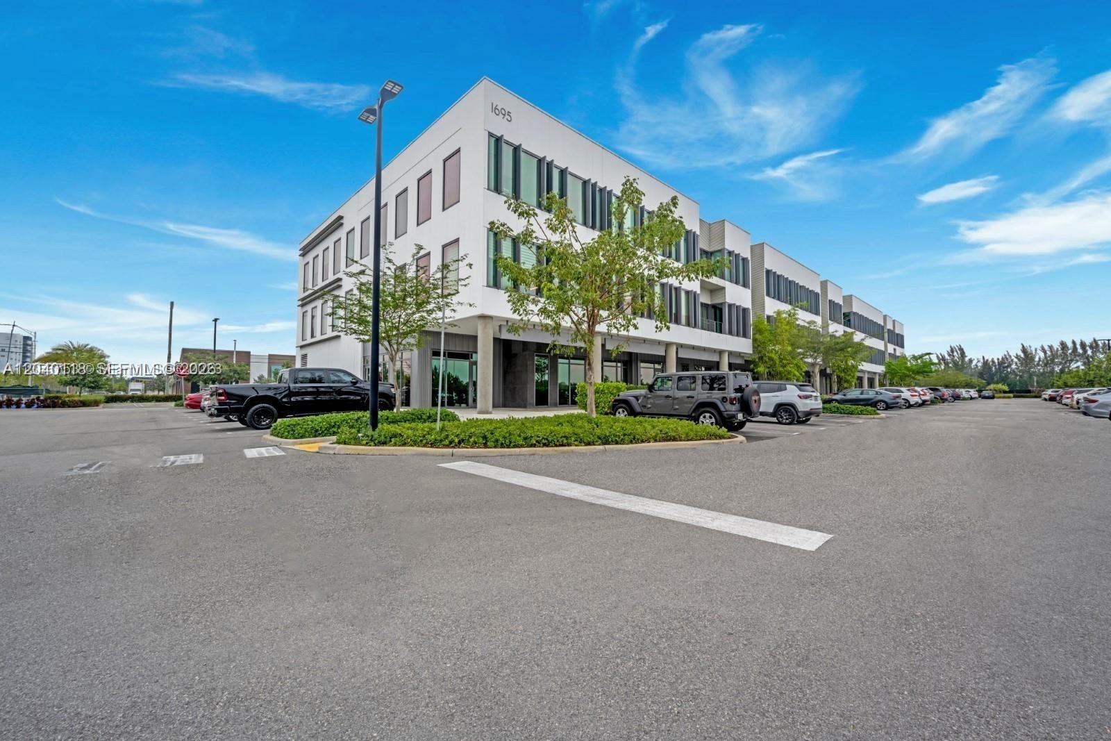 A modern three-story commercial building features a white facade, large windows, and a parking lot — SWEETWATER, FL