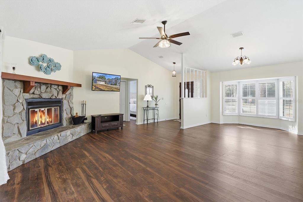 A spacious living room features a stone fireplace, dark wood flooring, and a vaulted ceiling — 4601 S GATOR LOOP, HOMOSASSA, FL