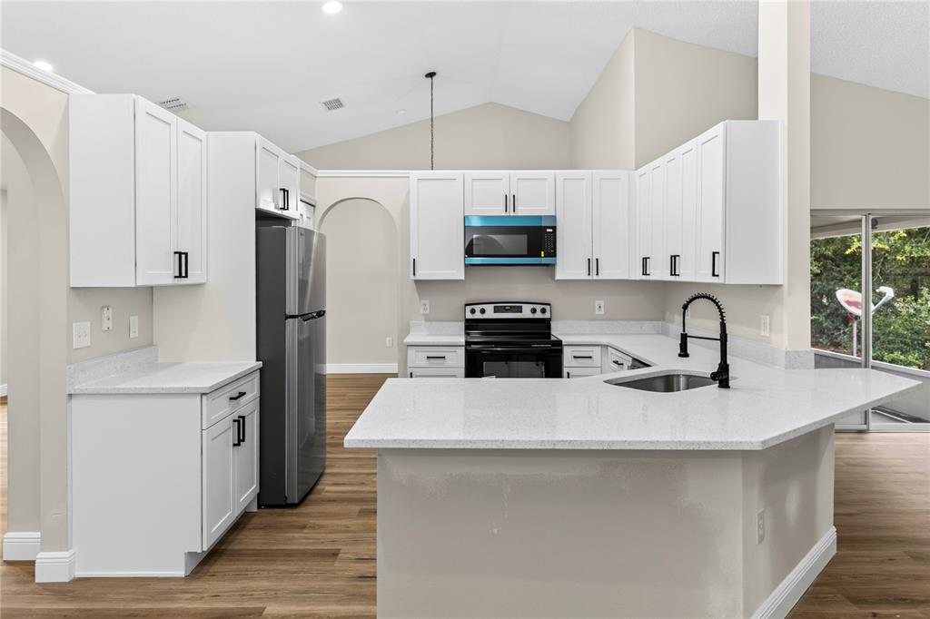 A kitchen features white cabinets, stainless steel appliances, a peninsula with a sink, and flooring — 2190 GLENLOCK DRIVE, DELTONA, FL
