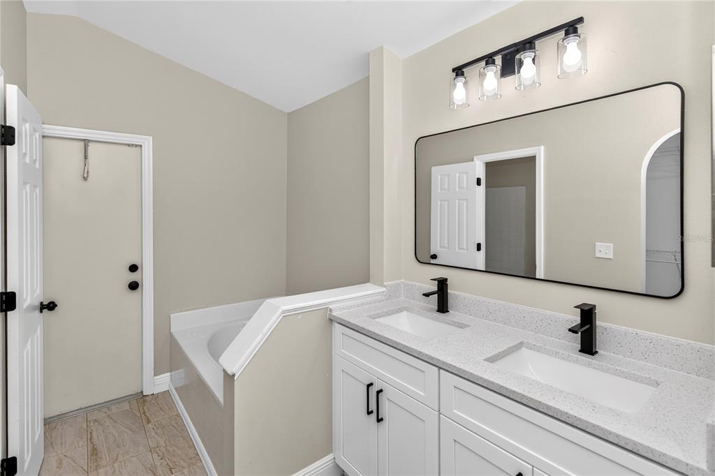 A bathroom features a double vanity with white cabinets, black fixtures, and a large wall mirror — 2190 GLENLOCK DRIVE, DELTONA, FL