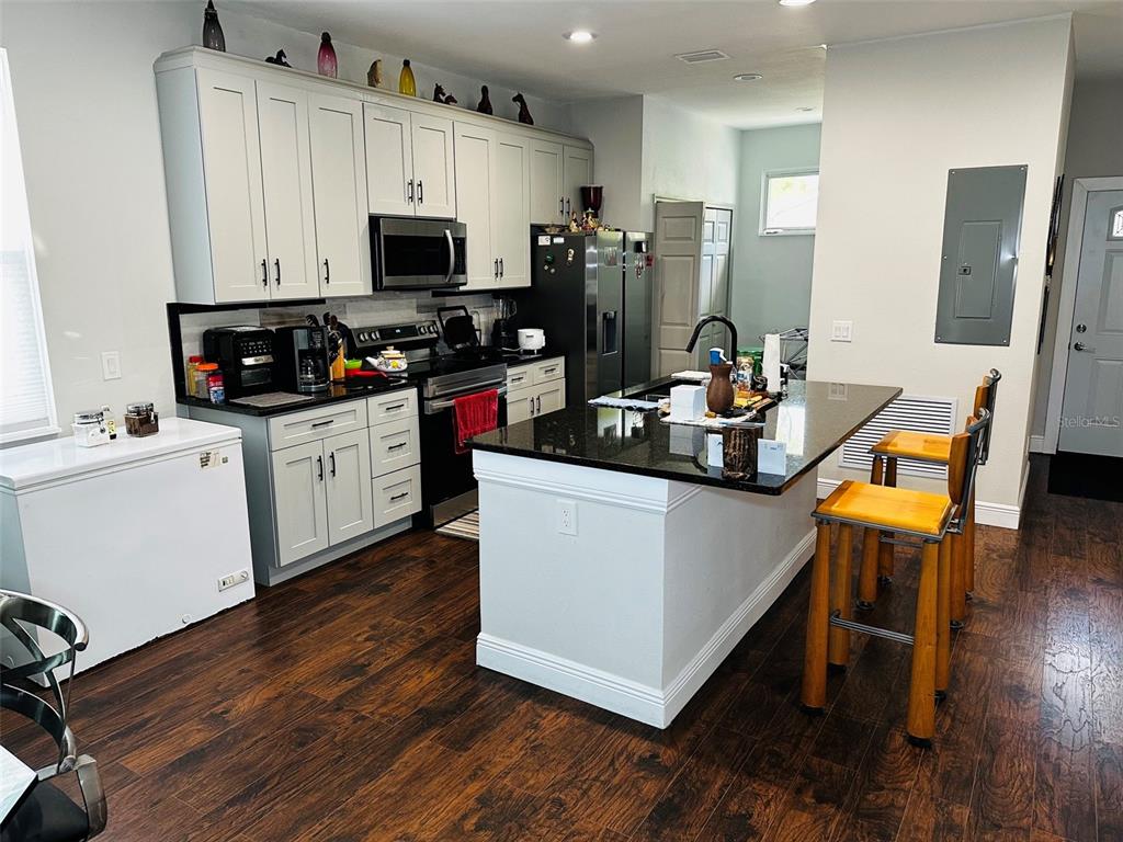 A kitchen features white cabinets, black countertops, a central island with bar stools, and wood-look flooring — 606 W VOORHIS AVENUE, DELAND, FL