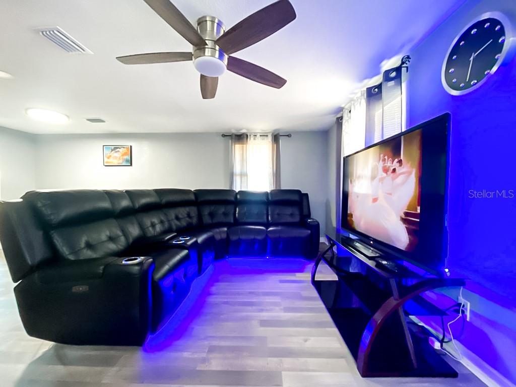 A living room features a black sectional sofa, a television on a stand, and blue lighting — 4303 CHESTNUT AVENUE, SARASOTA, FL