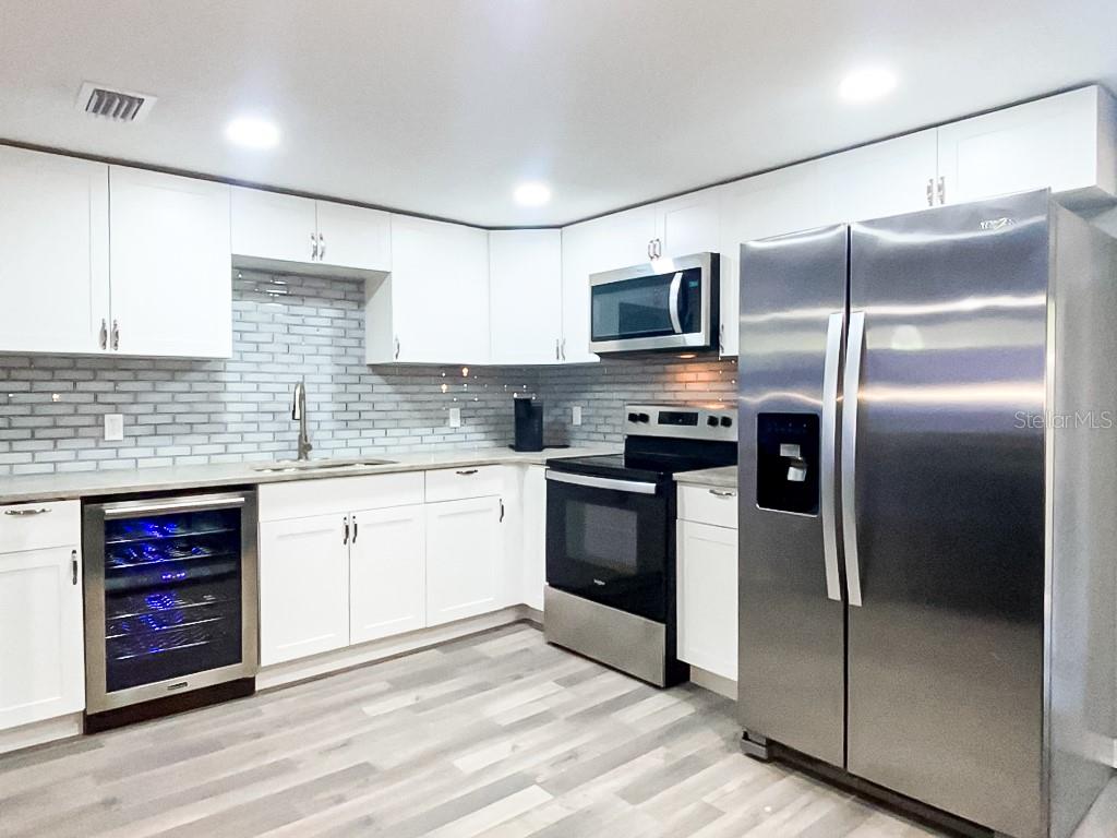 A modern kitchen features white cabinets, stainless steel appliances, a wine cooler, and gray flooring — 4303 CHESTNUT AVENUE, SARASOTA, FL