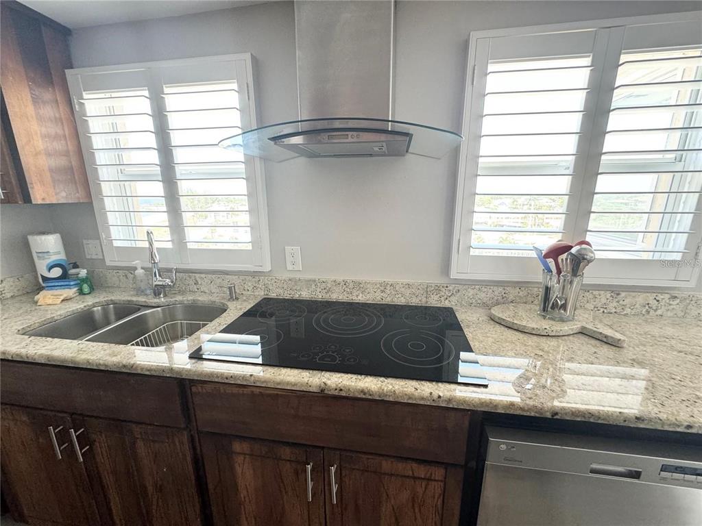 A kitchen features granite countertops, a glass-top stove, a stainless steel hood, and white shutters — 1255 TARPON CENTER DRIVE UNIT 612, VENICE, FL