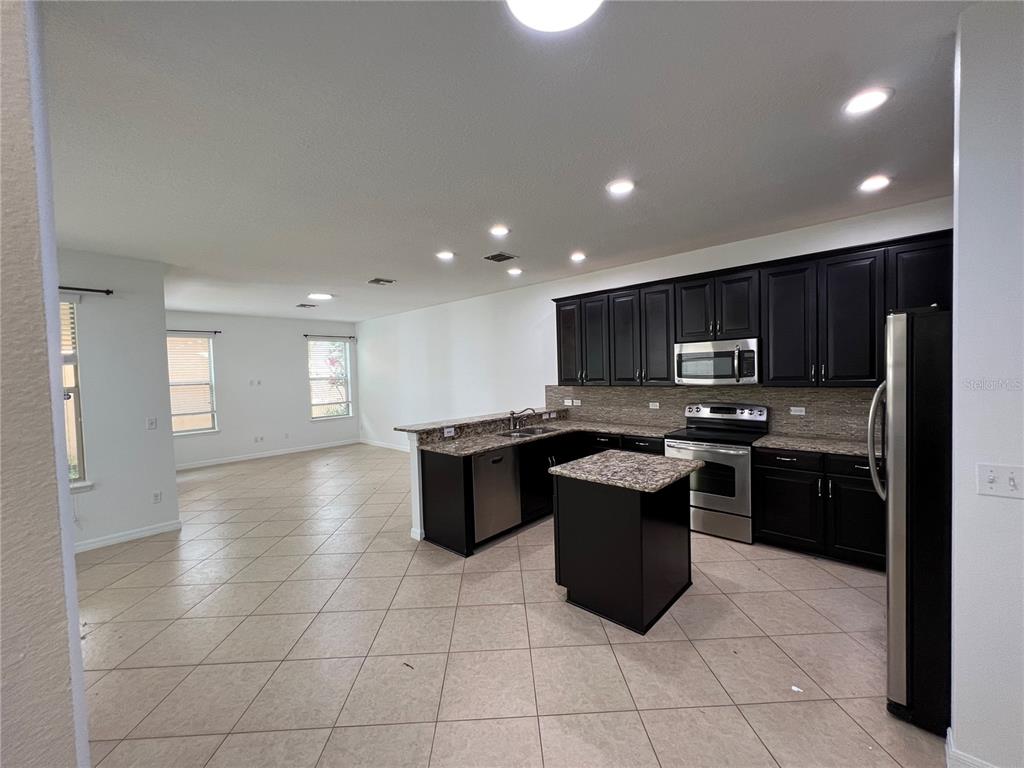 A kitchen with dark cabinets, granite countertops, and stainless steel appliances opens to a living area — 6526 GOLDEN DEWDROP TRAIL, WINDERMERE, FL