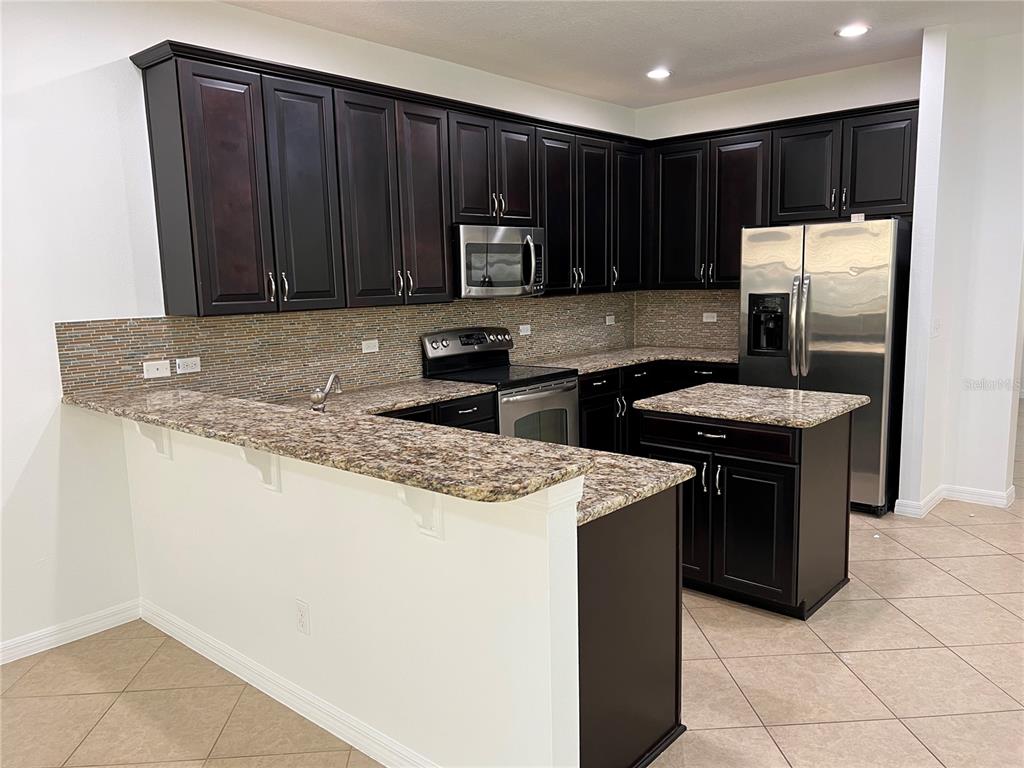 A kitchen features dark wood cabinets, granite countertops, stainless steel appliances, and a center island — 6526 GOLDEN DEWDROP TRAIL, WINDERMERE, FL