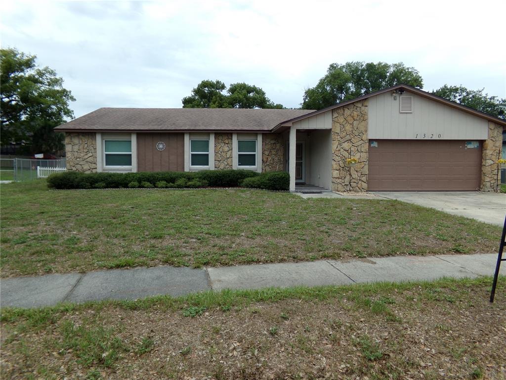 A single-story house features a stone facade, a brown garage door, and a grassy lawn — 1320 GLADIOLAS DR, WINTER PARK, FL