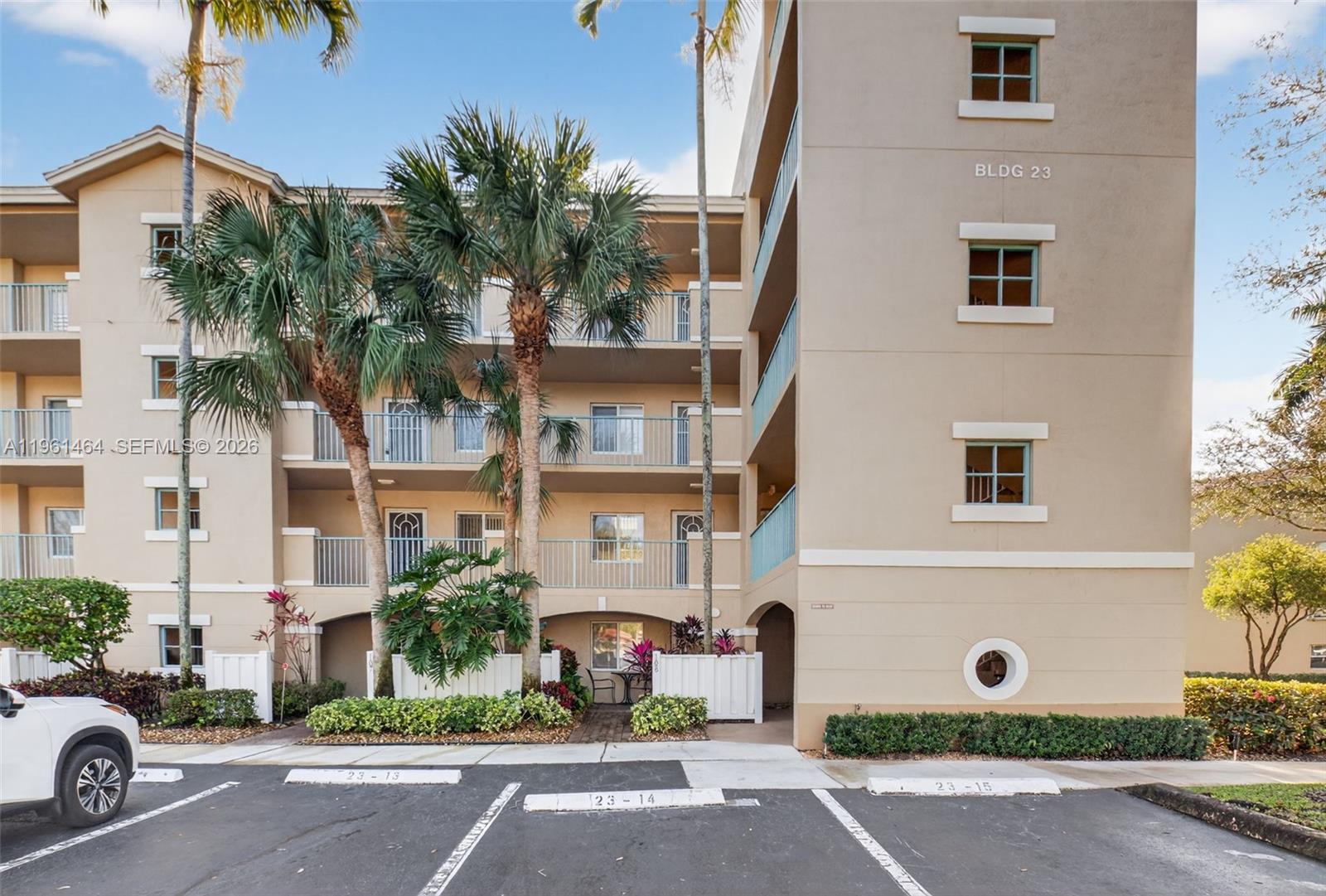 The exterior of a multi-story apartment building features balconies, palm trees, and marked parking spaces — 12540 Majesty Cir # 208, Boynton Beach FL 33437, BOYNTON BEACH, FL
