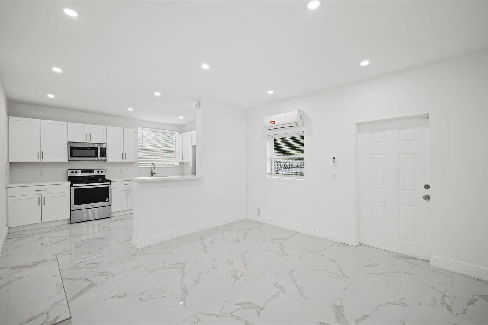 A bright kitchen and living area featuring white cabinets, stainless steel appliances, and marble-look flooring — 332 NW 97th Street, Miami FL 33150, MIAMI, FL