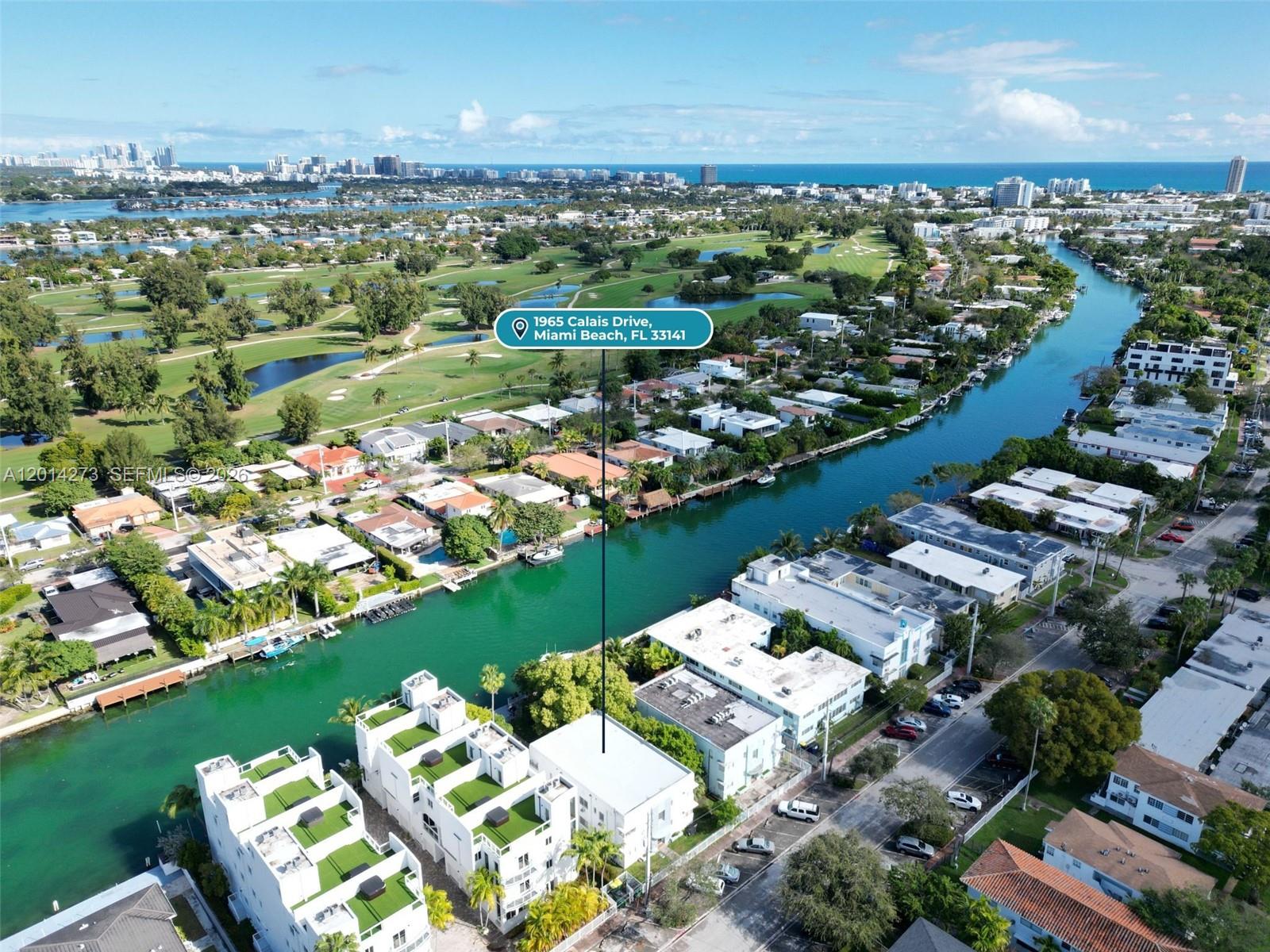 An aerial view shows a multi-story residential building situated along a canal near a golf course — 1965 Calais Dr # 7, Miami Beach FL 33141, MIAMI BEACH, FL