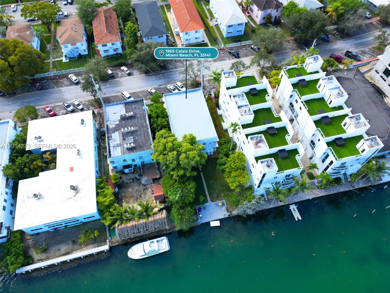 An aerial view shows a multi-story building with a flat roof situated along a canal — 1965 Calais Dr # 7, Miami Beach FL 33141, MIAMI BEACH, FL