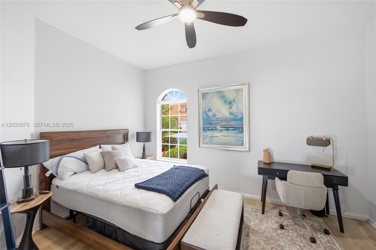 A bedroom features a wooden bed frame, a desk with a chair, and an arched window — 8141 Sandpiper Way, West Palm Beach FL 33412, WEST PALM BEACH, FL