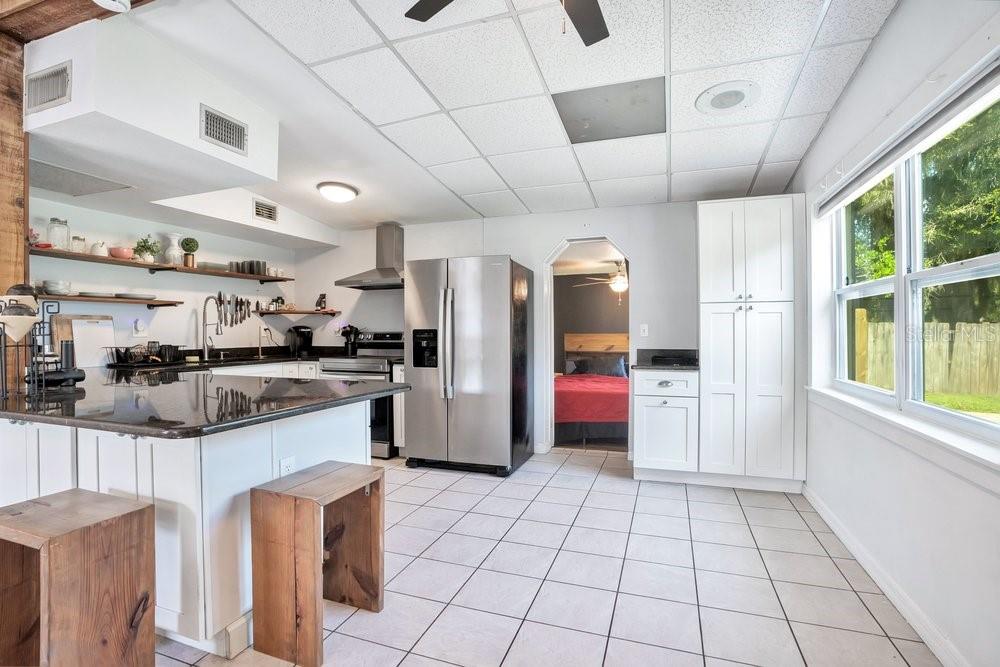 A kitchen with white cabinets, stainless steel appliances, a granite island, and tiled flooring — 310 E 6TH STREET, CHULUOTA, FL