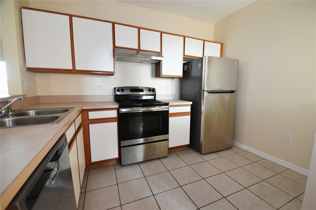 A kitchen features white cabinets with wood trim, stainless steel appliances, and tiled flooring — 9612 SEADALE COURT UNIT 201, RIVERVIEW, FL