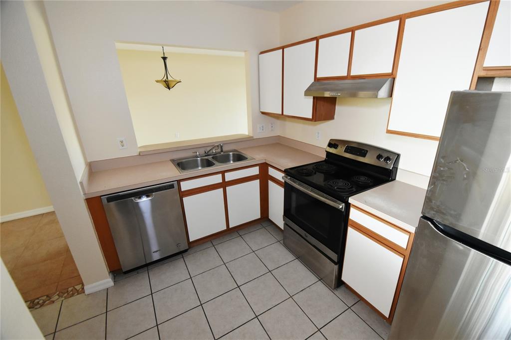 A kitchen features white cabinets, stainless steel appliances, tan countertops, and light-colored tile flooring — 9612 SEADALE COURT UNIT 201, RIVERVIEW, FL