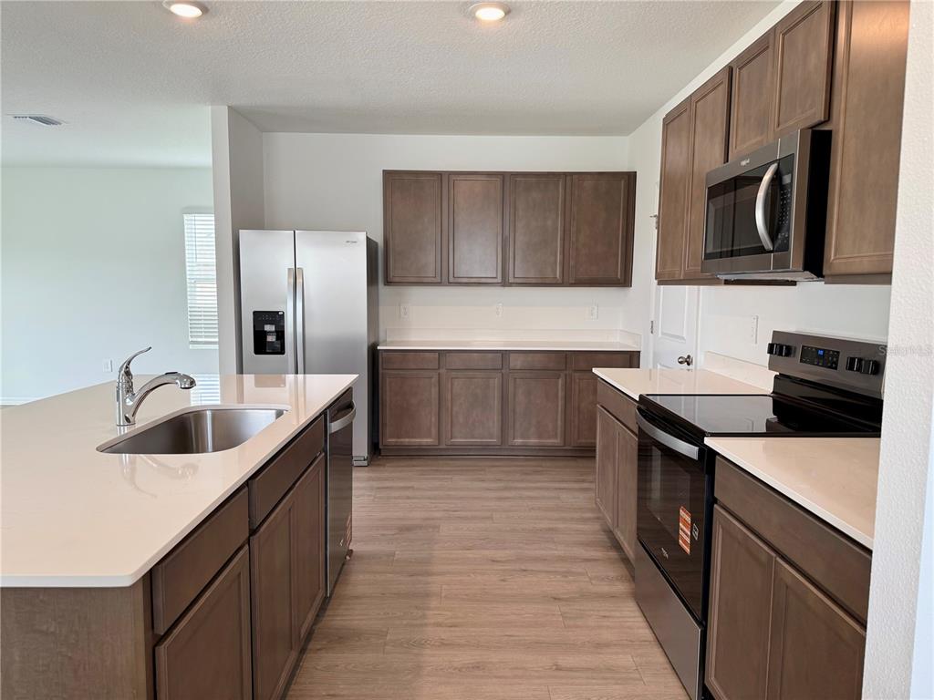A kitchen with wood cabinets, stainless steel appliances, and a large island with a sink — 35477 BRICK CHURCH LOOP, DADE CITY, FL