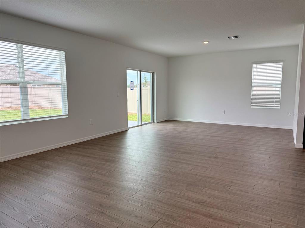 An empty living room features light wood-look flooring, white walls, and a sliding glass door — 35477 BRICK CHURCH LOOP, DADE CITY, FL
