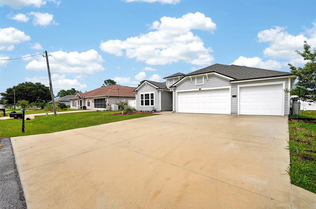 A gray house with a three-car garage and a large concrete driveway under a sky — 21 ROCKING LANE, PALM COAST, FL