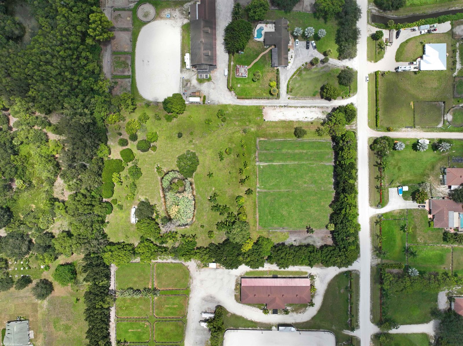 This aerial view shows a rural property with multiple buildings, fenced pastures, and dense trees — 16639 Hollow Tree Lane, Wellington FL 33470, WELLINGTON, FL